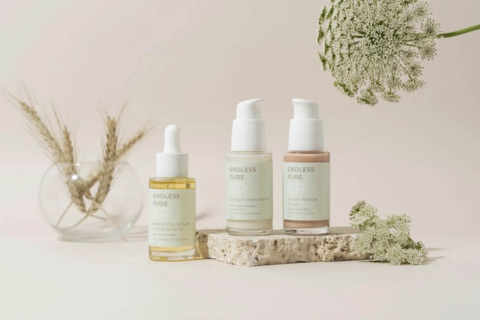 Serum and lotion bottles on a stone slab with dried flowers, illustrating the Alaikas.com skincare routine