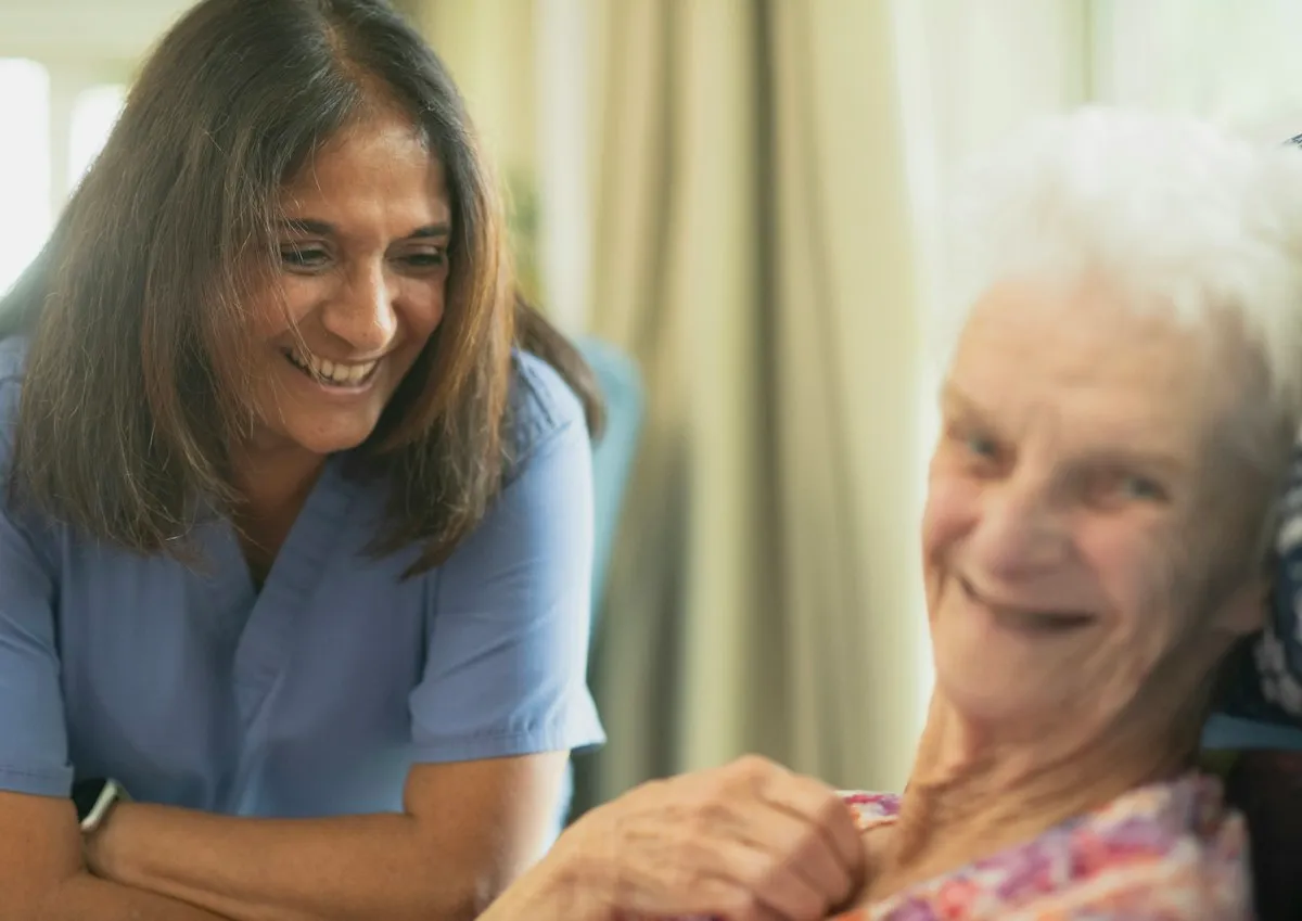 Smiling caregiver sitting beside an elderly woman and sharing a warm moment together