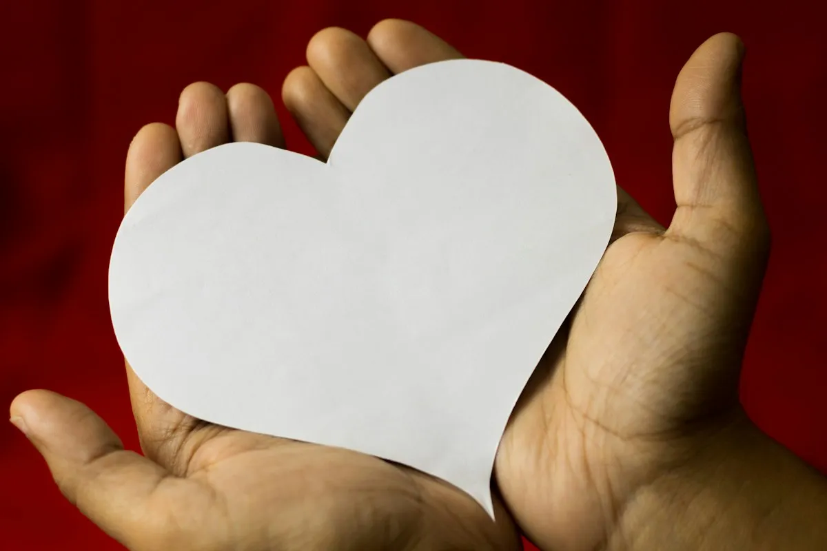 Hands holding a white paper heart against a bright red background, a symbol of heart health