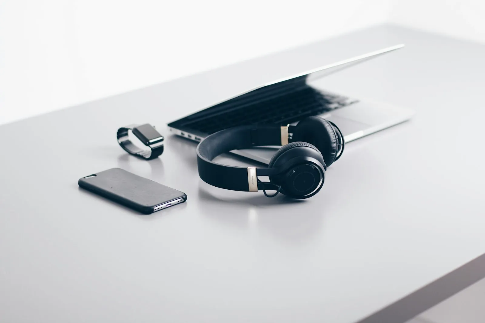 Wireless headphones, smartphone and smartwatch beside a laptop on a white desk, from Alaikas.com tech accessories