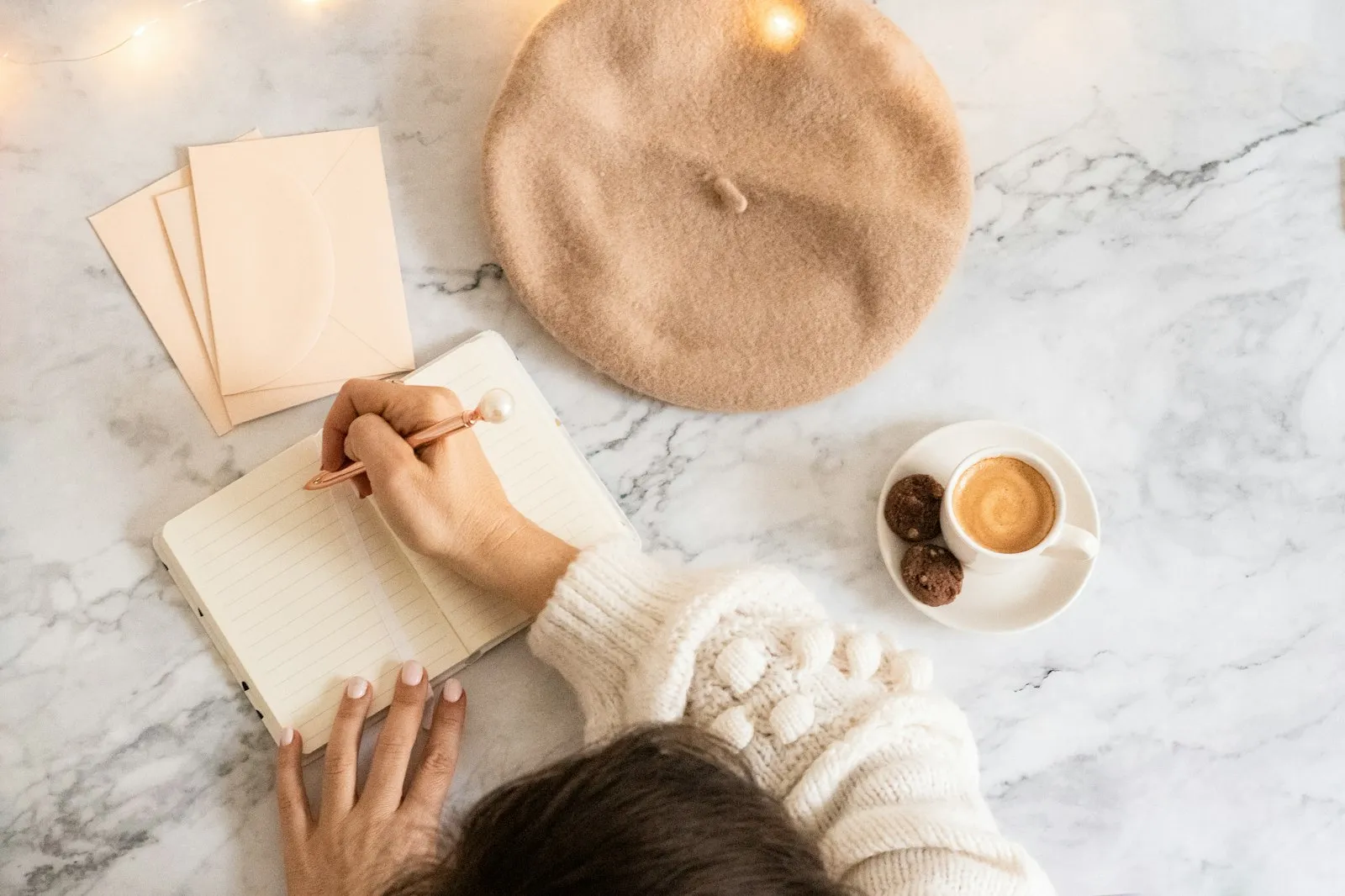 Woman writing in a journal beside a coffee on a marble table, an Alaikas.com daily habits idea
