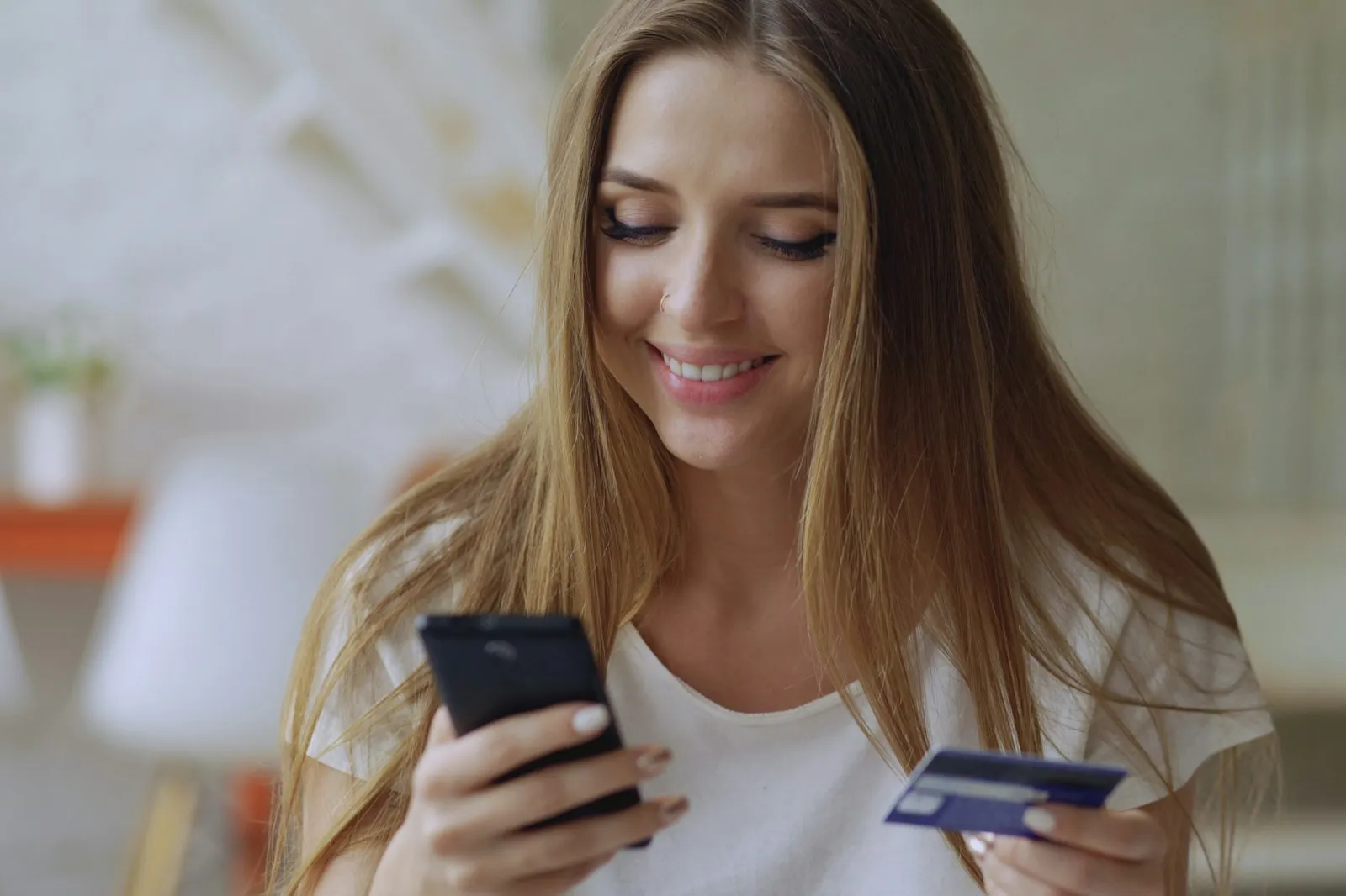 Smiling woman holding a smartphone and credit card while shopping safely online with Alaikas.com picks