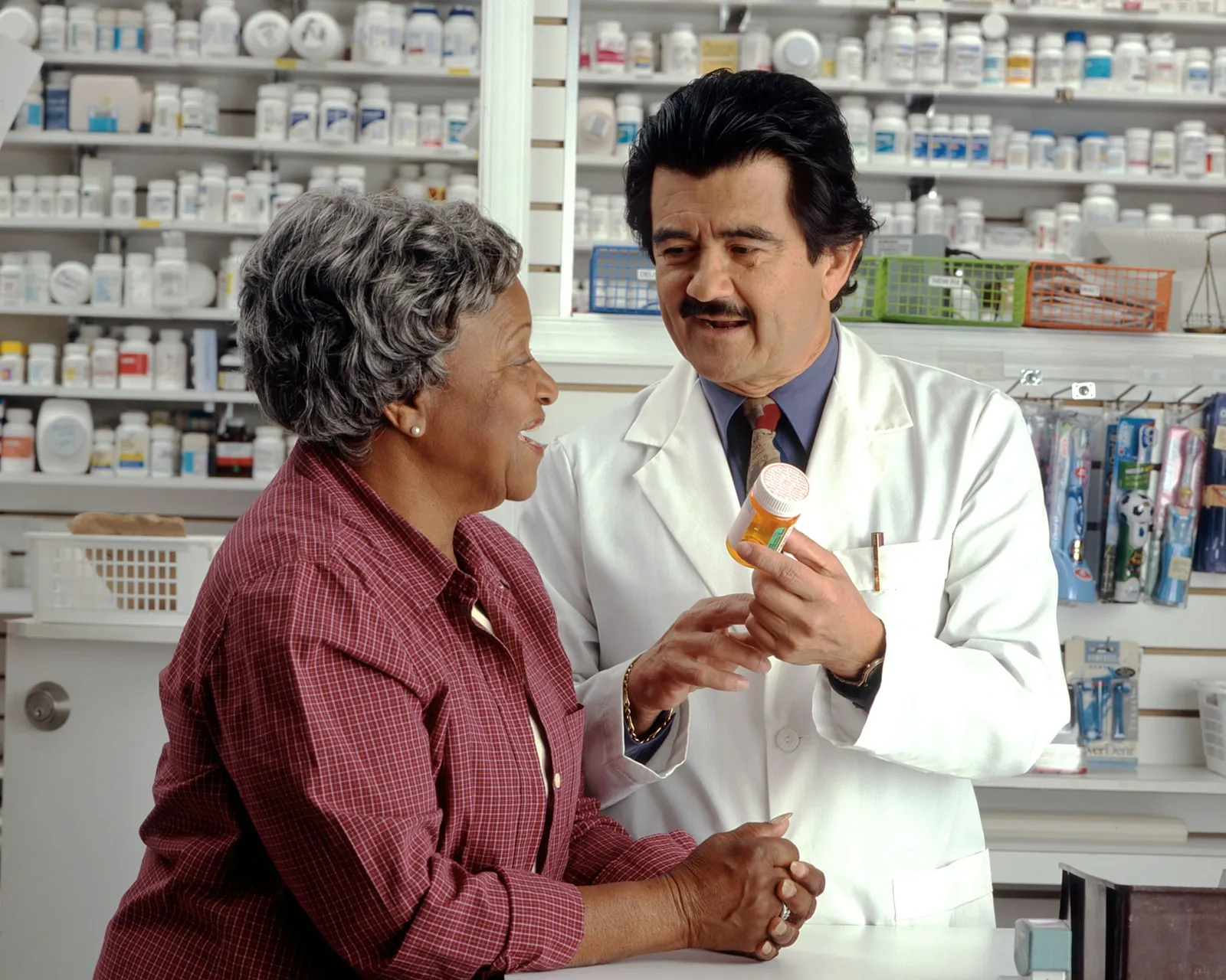 Pharmacist explaining a prescription and medication instructions to an older patient at the pharmacy counter
