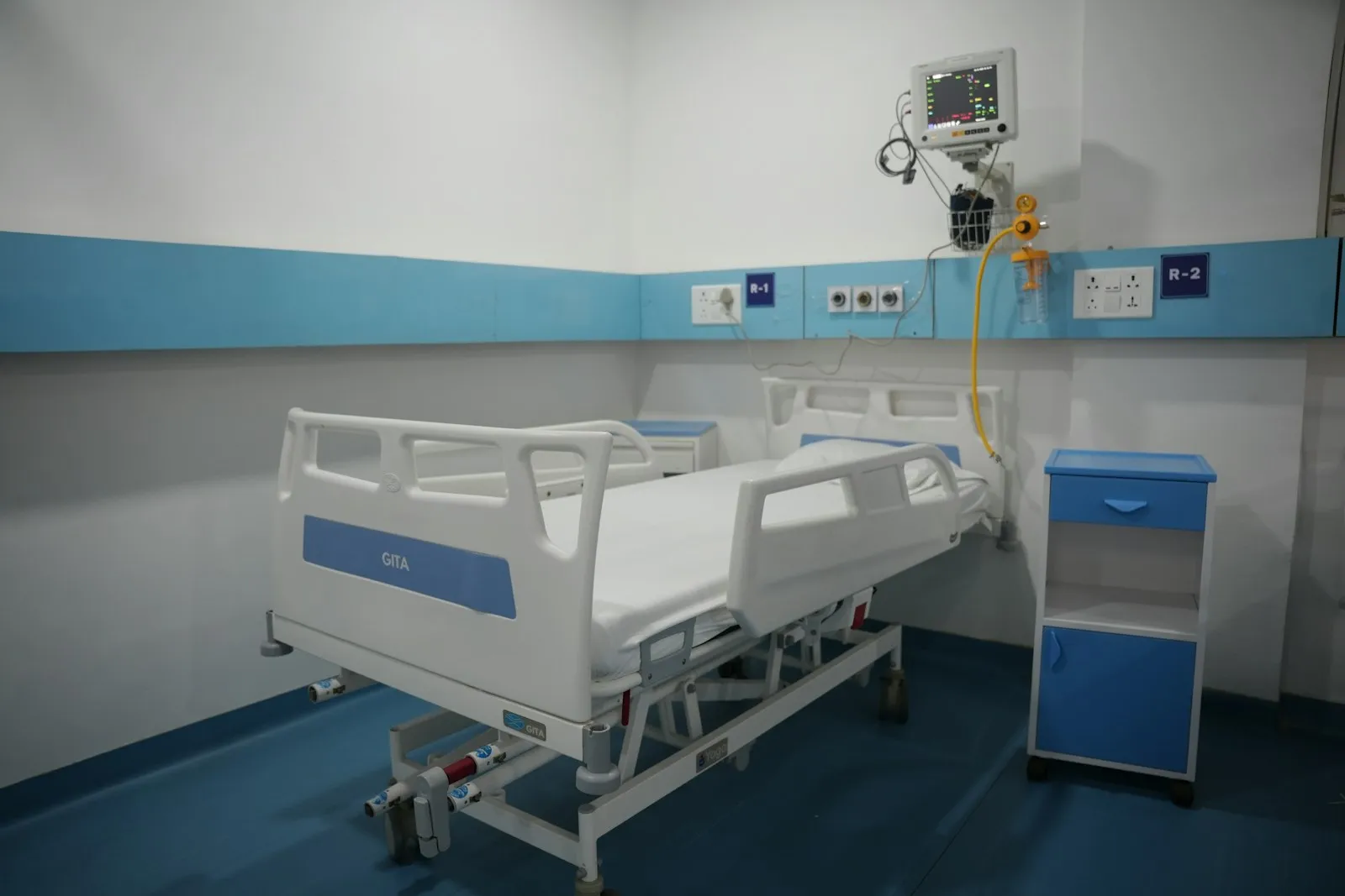 Modern private hospital room with an adjustable patient bed, bedside cabinet and visitor chair