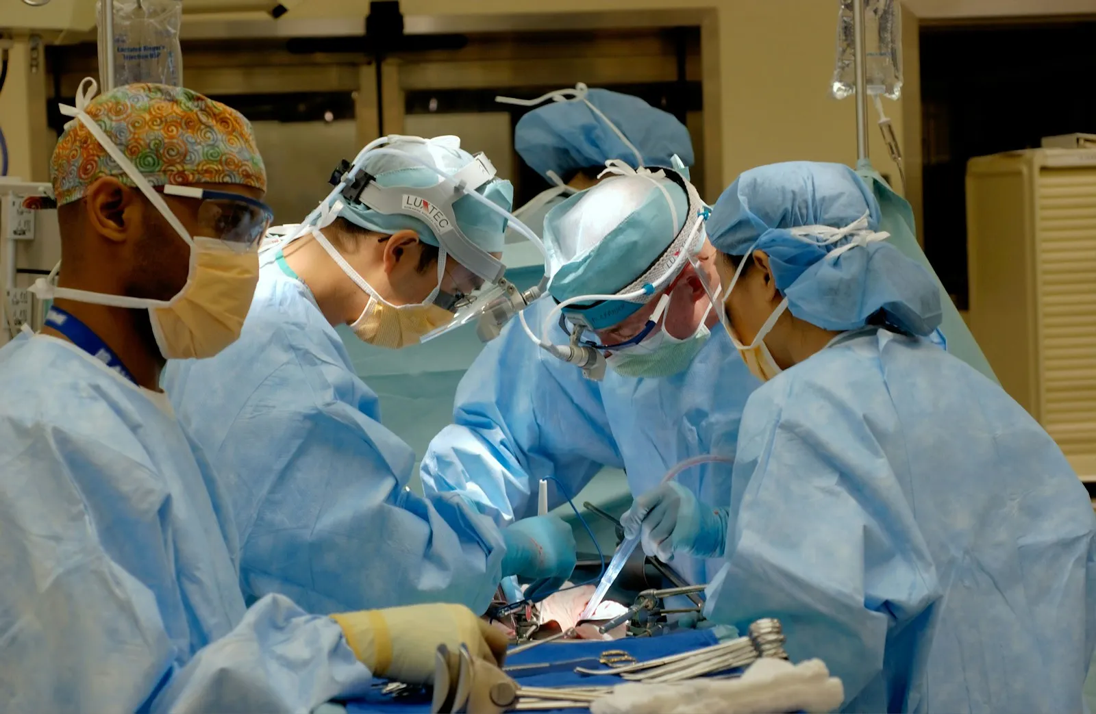 Team of four surgeons in scrubs and masks performing an operation in a bright operating room