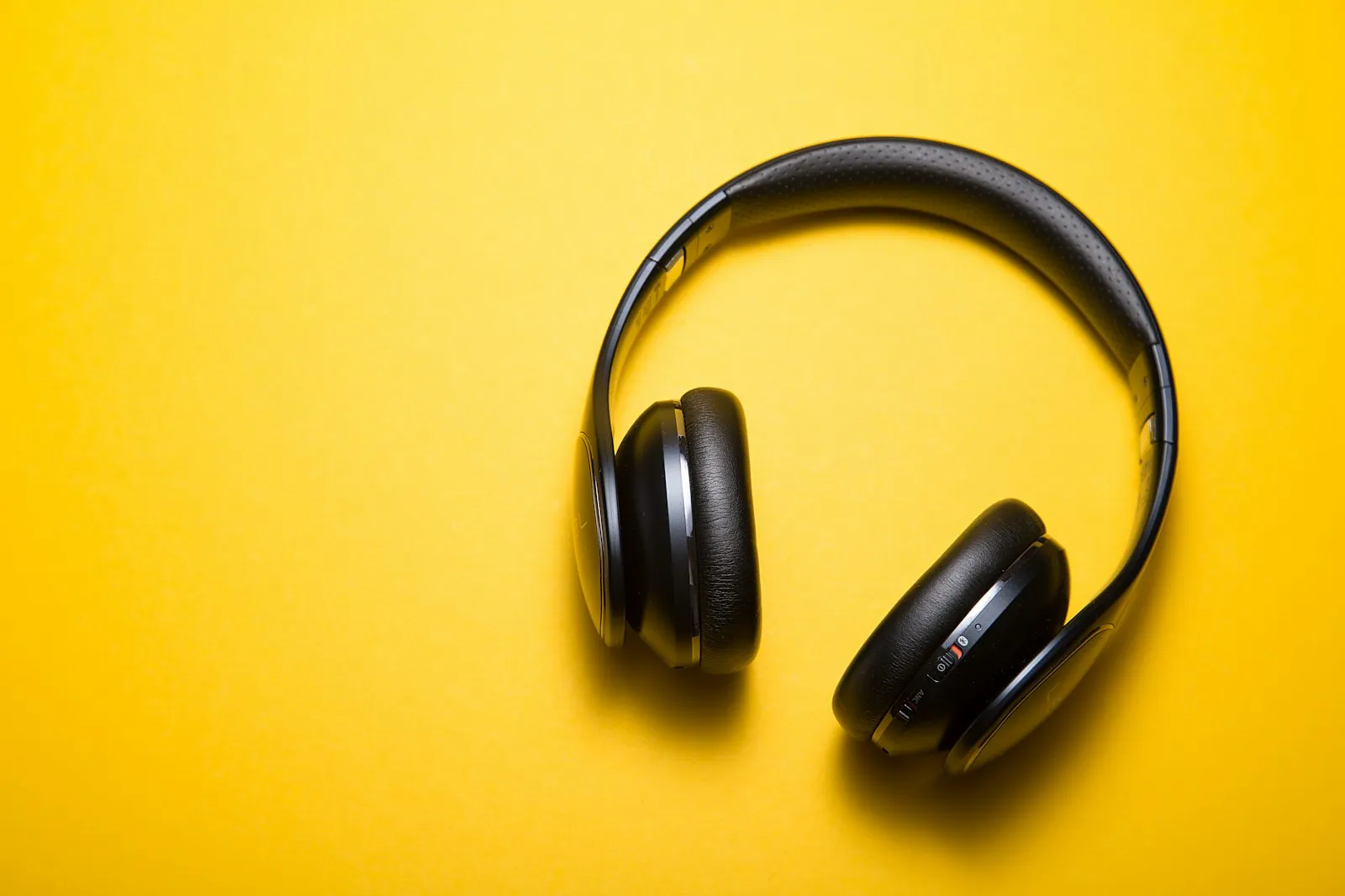 Black over-ear wireless headphones on a yellow background, from the Alaikas.com audio gear guide