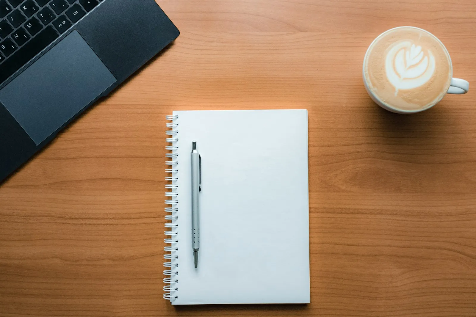 Blank spiral notebook and pen beside a latte and laptop, from the Alaikas.com content writing guide